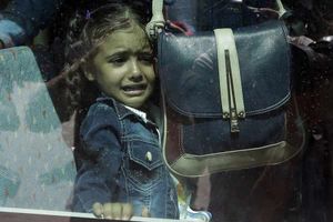 A girl cries as she waits on a bus which will transport her family to the metro station in Lesbos