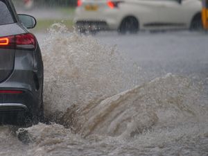Cars drive through a flooded road after heavy rain.