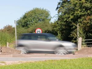 A silver car, blurred by speed, passes a circular No Cars road sign