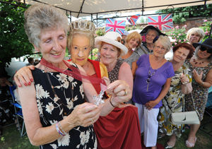 Jean Hughes (left) at a celebration garden party to honour her forthcoming British Empire Medal, with a mock medal from the "Queen" and Ann Bedworth (white hat) along with other attendees
