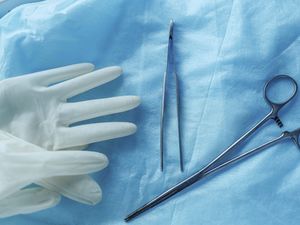 A stock image of surgical tools and gloves on blue cloth, showing readiness for medical procedures