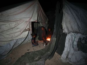 A displaced family sit round the fire in their tent at a camp in Deir al-Balah, Gaza Strip