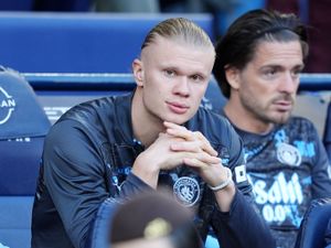 Erling Haaland, with his chin resting on his hands, sits on the Manchester City bench