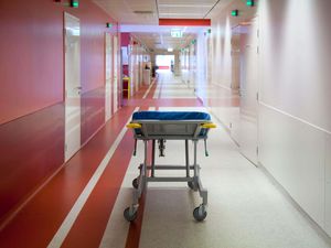 Corridor and waiting areas of a modern hospital with seating, a trolley bed with blue mattress