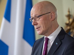 John Swinney speaking, with a Scottish flag in the background