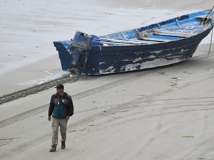 Man walks along beach away from blue boat