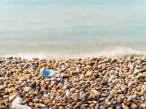 A plastic bottle on a pebble beach with the sea behind