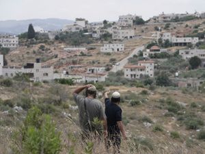 Israeli settlers look towards their neighbouring village