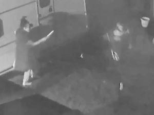 Black and white still from cctv showing a woman standing next to a caravan holding a knife