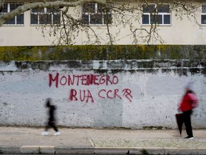 People walk past graffiti on a wall in Lisbon saying 'Montenegro out'