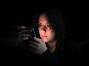 A young girl in the dark staring into her mobile phone