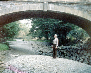 Peter Watkin standing on the dry river bed of the Rhiew at the Revel Bridge during the drought, August 1976. The dry river bed reached up to the Berriew village bridge.