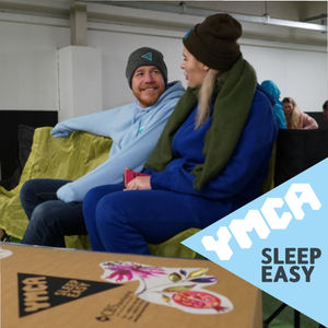 Two people dressed warmly huddled by a cardboard box whilst sleeping out