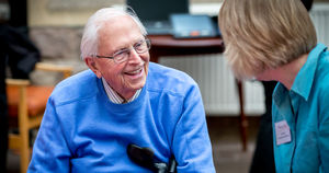 An elderly man in a blue jumper and glasses chats to a volunteer at a sight loss event.