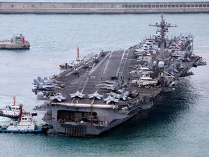 Aerial view of the USS Carl Vinson being ushered into port by tugs