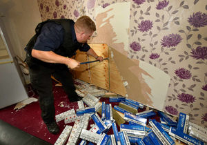 Dog handler Stuart Phillips looks behind the fake wall, after finding a large amount of illicit cigarettes under it