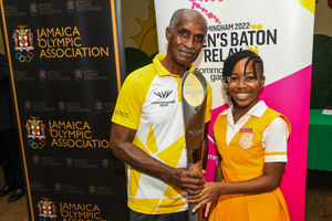 1976 Olympic Gold Medallist Don Quarrie holds the baton alongside a school student in Jamaica
