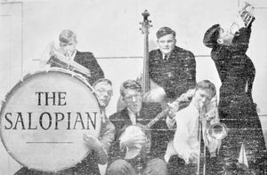 Laurence Le Quesne playing the drum with The Salopian band. Behind him is Malcolm Mitchell, playing banjo is Willie Rushton and behind with the double bass is "Jones" with Christopher Booker playing the trombone and in profile on the right, Paul Foot. 
