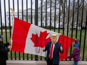 A Toronto man and his son hold a Canadian flag in front of the White House in Washington DC as another visitor to the city wears a Donald Trump mask