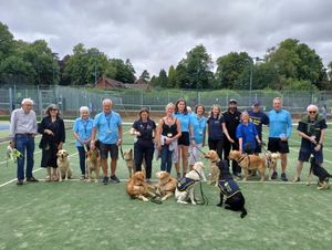 A group shot of tennis club members and Guide Dogs volunteers with dogs. 