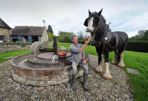 Wagoner Simon Trueman, with 'Alfie', next to the stone cider mill, at Acott Scott Historic Working Farm.