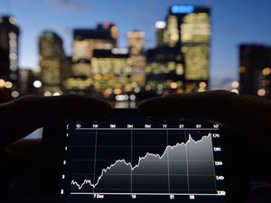 A person views share prices on an Iphone, with London’s Canary Wharf in the background