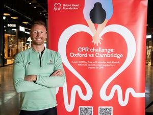 Cambridge rower James Robson stands beside a British Heart Foundation sign