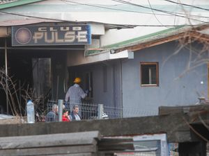 People outside a burnt-out building, which has a sign on it reading 'Club Pulse'