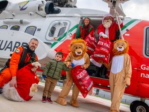 Santa, lion helpers, a Coast Guard member and an elf drop off sacks of toys at a hospital from e helicopter