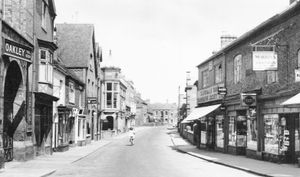 A real photographic postcard picture of Cheshire Street, Market Drayton in 1962. This was shared by Dave Francis: 'The postcard, which is at least 55 years old, was posted to an address in Plymouth, Devon. If only Cheshire Street was as quiet nowadays although the photographer must have taken this photo early in the morning sun as only one female cyclist can be seen pedalling away from us. On the left Oakleys agricultural shop and yard can be seen followed by The Oak pub and Town Hall on the left with its unusual domed top. Way in the centre distance the Railway Hotel can be discerned. On the right foreground Morris's tobacconists can be seen advertising Gold Flake and Players Nun tobacco followed by Beresfords cycle shop showing signs for Rudge cycles, Michelin cycle tyres and Exide batteries. The last shop on the right is the Silverdale Cooperative Society Ltd. For those of you with a keen eye an old fashioned telephone box is located to the left of the cyclist at the entrance to the Oak yard which led to the old covered market. Sadly all these premises I have mentioned have long since gone, said Dave Francis.'