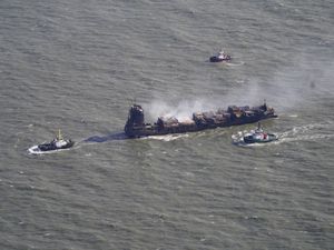 Aerial view of the Solong smoking, with three tugs alongside it