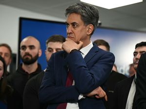 Ed Miliband with one hand resting on his chin, standing amongst a group of people