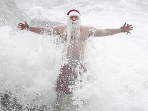 Waves crash over a sea swimmer dressed in a Santa hat and beard