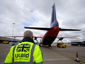 Shot of a runway showing a man in a high viz jacket with the UK Aid logo on it looking at the back of a plane