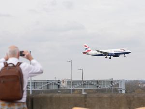 A plane spotter with binoculars from behind watching a British Airways plane landing
