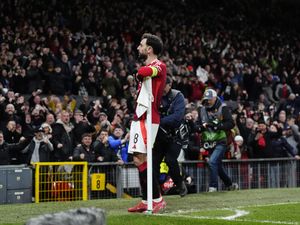 Bruno Fernandes stands with his arm resting on the corner flag facing the Manchester United fans in celebration