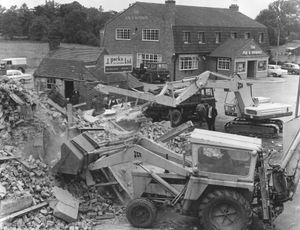 'The diggers moves in and the old Fox and Hounds at Shawbury comes down on August 11, 1966. Demolition work started on the pub this day using a new technique, with a demolition arm attached to a machine crashing down on the building. In the background is the new Fox and Hounds pub which was opened in April 1966.