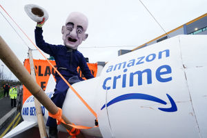 An activist from Extinction Rebellion, wearing a giant Jeff Bezos head, blocks the entrance to the Amazon fulfilment centre in Tilbury