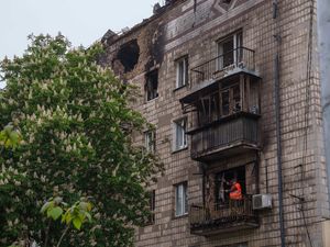A municipal worker clears rubble from a balcony after a Russian strike in Kyiv