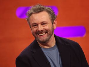 Michael Sheen smiling, with red and purple background