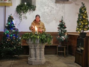 Reverend Rachael Storer lighting a candle in the church surrounded by trees in the festival.