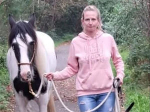 Leanne Williams wearing a pink hoodie and leading a white horse with black markings