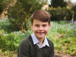 Prince Louis smiling as he poses for a photo against a woodland backdrop