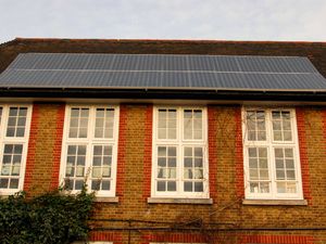 Solar panels on the roof of an old brick school with high windows