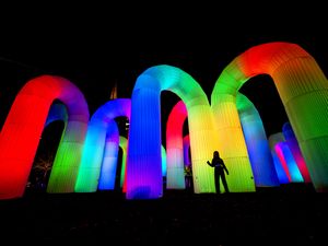 A person standing in front of large inflatable arches, which are multicoloured