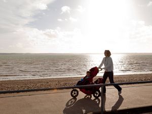 Mother and children with pushchair walking on promenade with sea as background