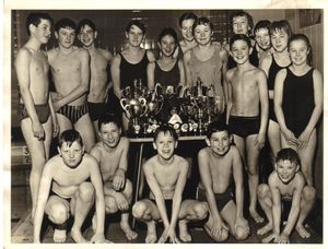 Brierley Hill Amateur Swimming Club members with their haul of trophies in December 1964: Back – Michael Dunn, Michael Palmer, Mike Overton, Irene Crombie, Lynne Ford, Ann Udall, Katie Tunnicliffe, Rosie Bowen, Liz Brown, Gayle Marklew, Carol Thatcher; next to table – Clive Davies; Front – John Howells, Chris Harris, Kevin Marklew, David Brown, Barry Davies.