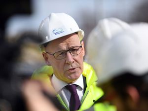 John Swinney speaking while wearing a white hardhat and yellow hi-viz jacket