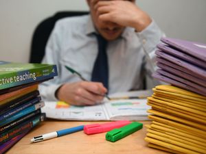 A primary school teacher looking stressed next to piles of classroom books