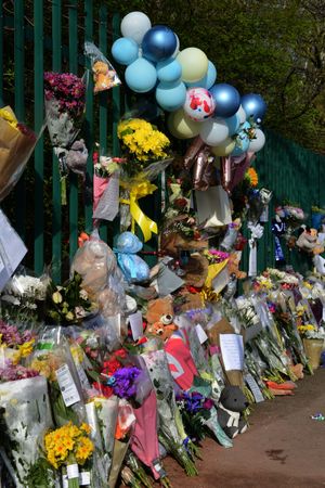Balloons have been tied to a fence and flowers laid